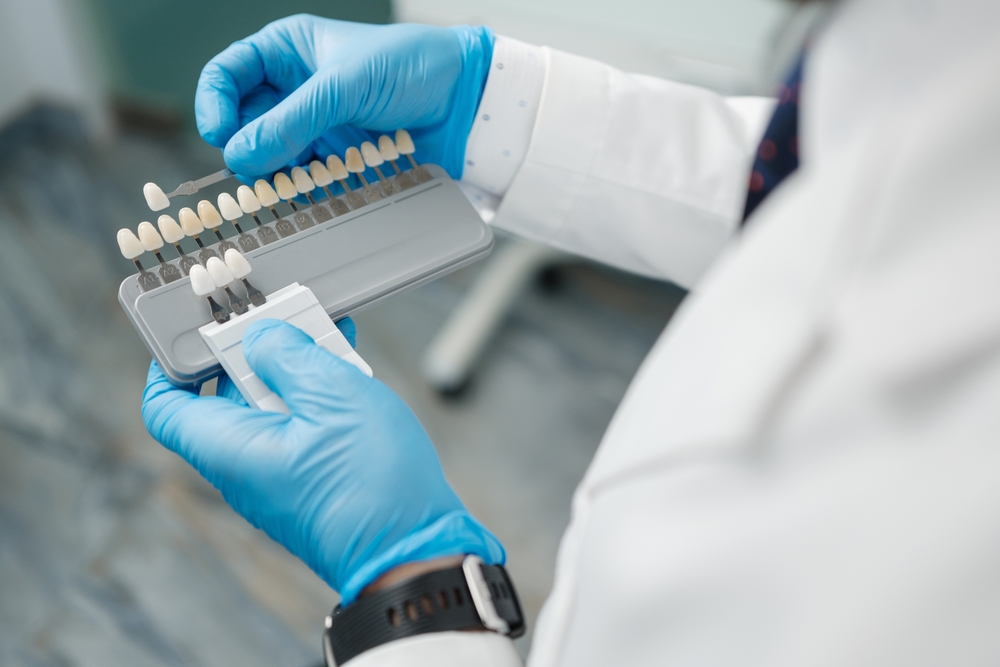 A dental professional wearing gloves holds a porcelain veneer shade guide, selecting a match for the patient – Veneers