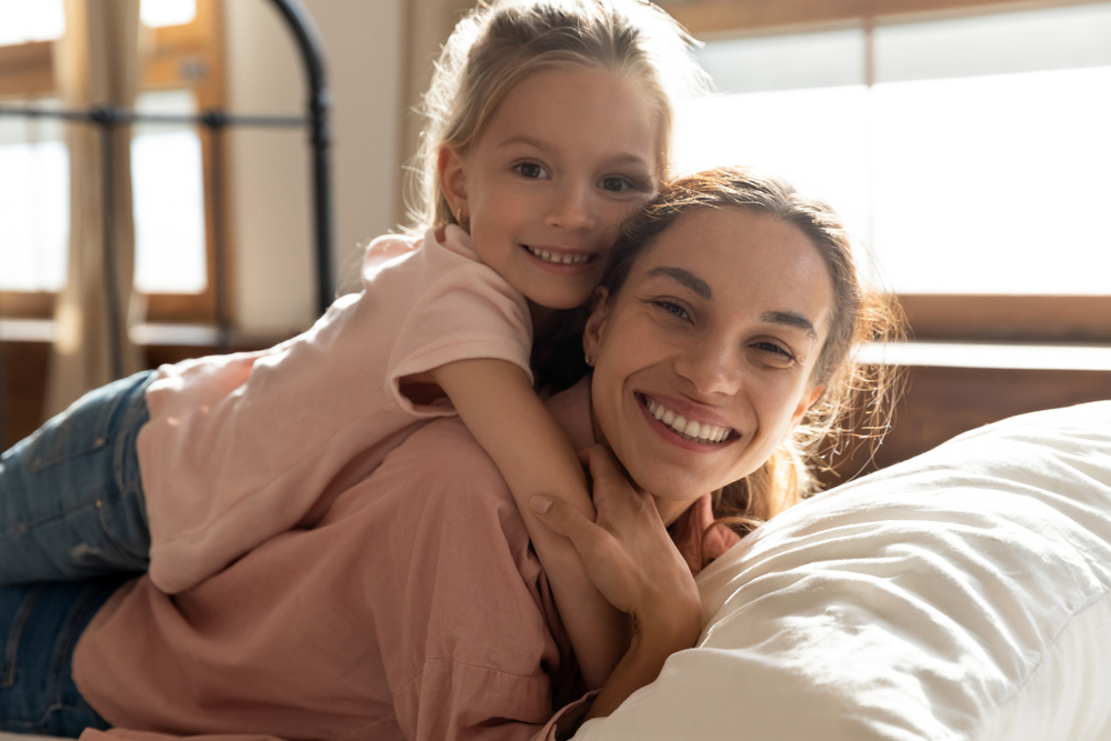 A joyful mother and daughter smiling and embracing each other in a bright room, showcasing healthy teeth and bonding moments – Dental Bonding