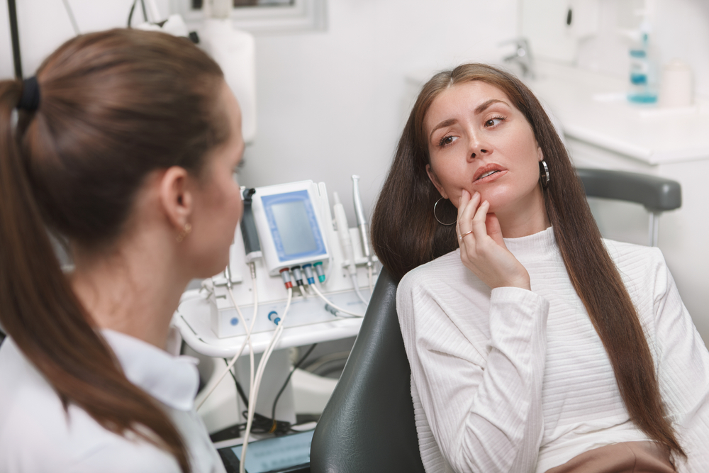 A patient seated in a dental chair, discussing a toothache with a dentist  A patient seated in a dental chair, discussing a toothache with a dentist