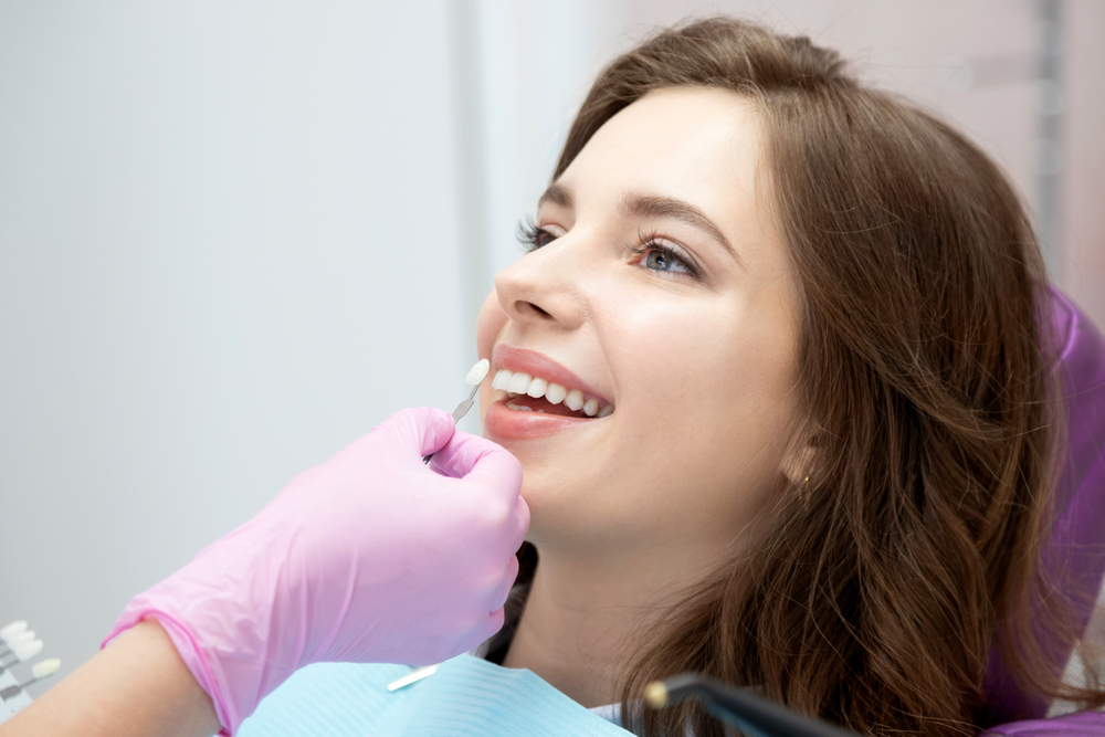 Patient Undergoing Veneer Shade Matching at Dental Visit – Dentist Orting WA A smiling woman reclines in a dental chair while a gloved hand holds a veneer shade guide to her teeth for cosmetic color matching – Dentist Orting WA