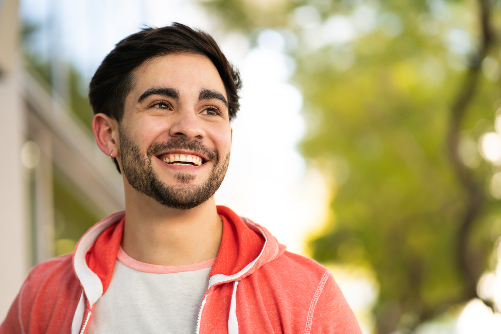 Confident Young Man Smiling Outdoors – General Dentistry A happy young man in a red hoodie smiling outside, showing healthy teeth maintained through general dentistry – General Dentistry