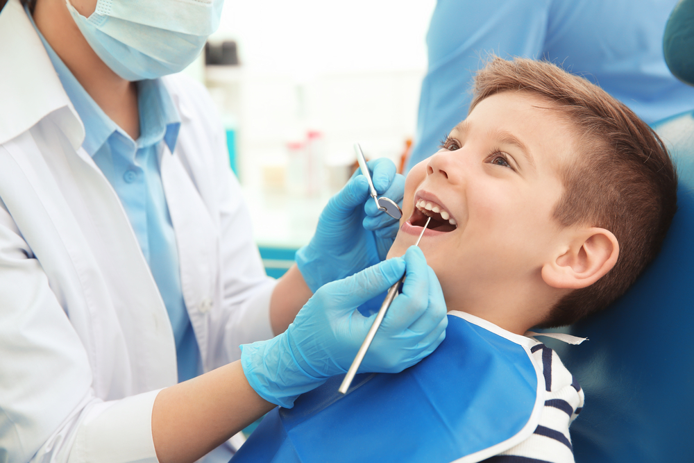  A cheerful young boy being examined by a dentist with gloved hands, possibly during or before a dental extraction – Extractions