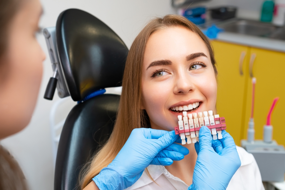 A dentist holds a shade guide up to a young woman’s teeth to select the right color for dental veneers – Veneers