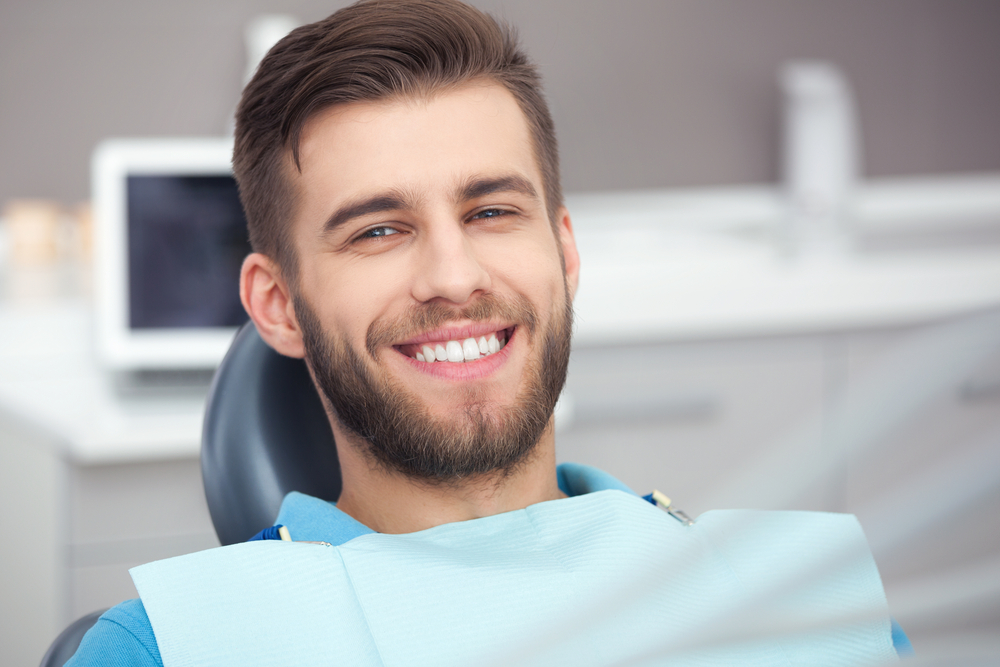 A smiling man seated in a dental chair, showing clean and restored teeth following a successful root canal treatment – Root Canals