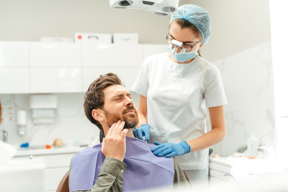 A man in a dental chair touching his jaw while a dental professional consults him, possibly evaluating teeth before whitening – Teeth Whitening
