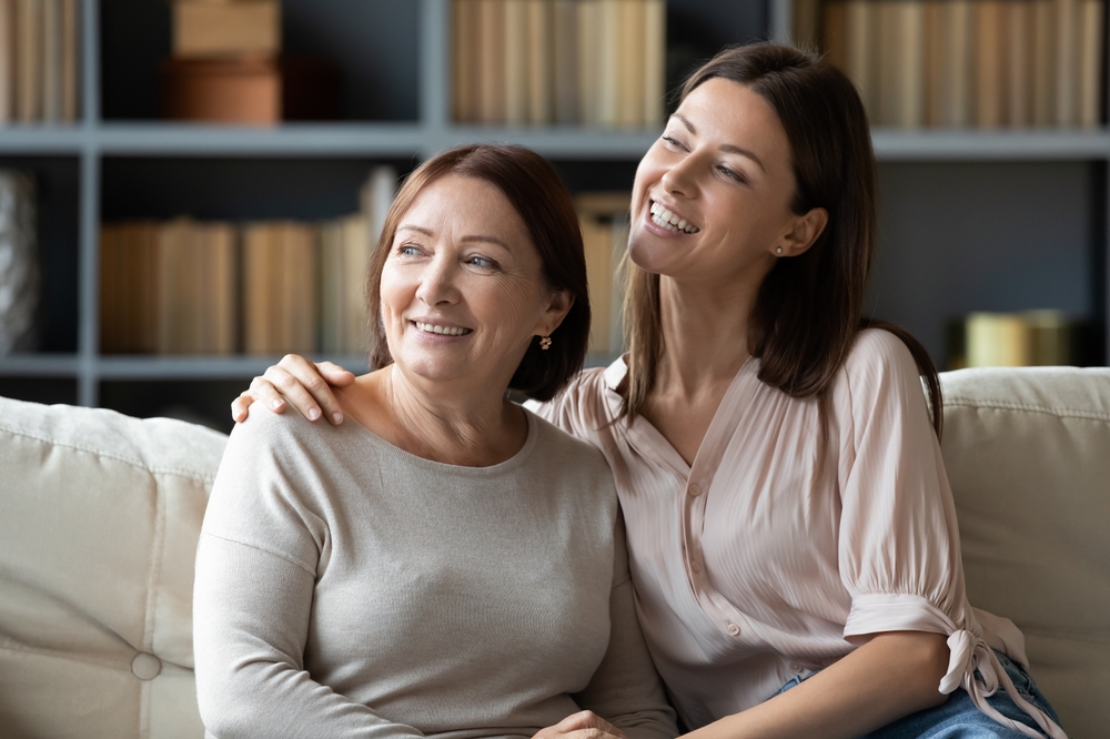 Happy Mother and Daughter Smiling Together at Home – Dental Crown A cheerful mother and daughter sitting on a couch, smiling and enjoying quality time together, showcasing healthy teeth after dental crown treatments – Dental Crown