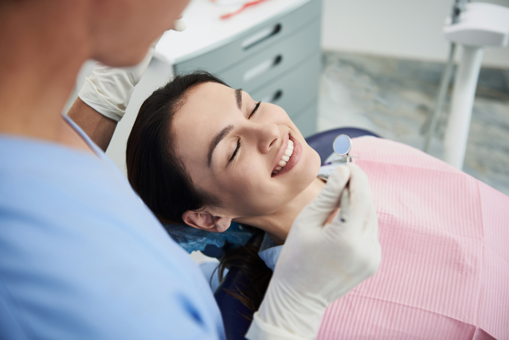 A woman in a dental chair smiling comfortably as a dentist examines her teeth, possibly during a root canal appointment – Root Canals