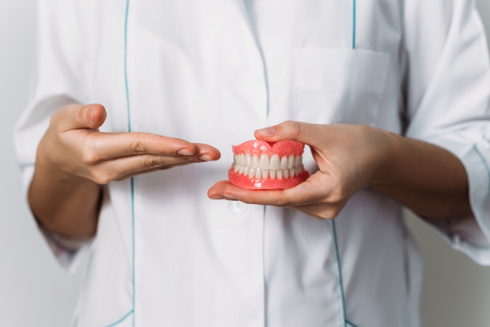 Dentist Showing Dental Implant Model to Patient – Dental Implants A dentist holding a model of a dental implant during a consultation, explaining the procedure to a patient in a clinical setting – Dental Implants