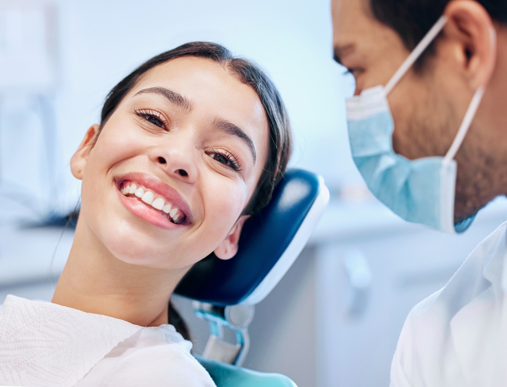 A young woman in a dental chair smiling with confidence, showing off her radiant teeth after a teeth whitening treatment – Teeth Whitening 